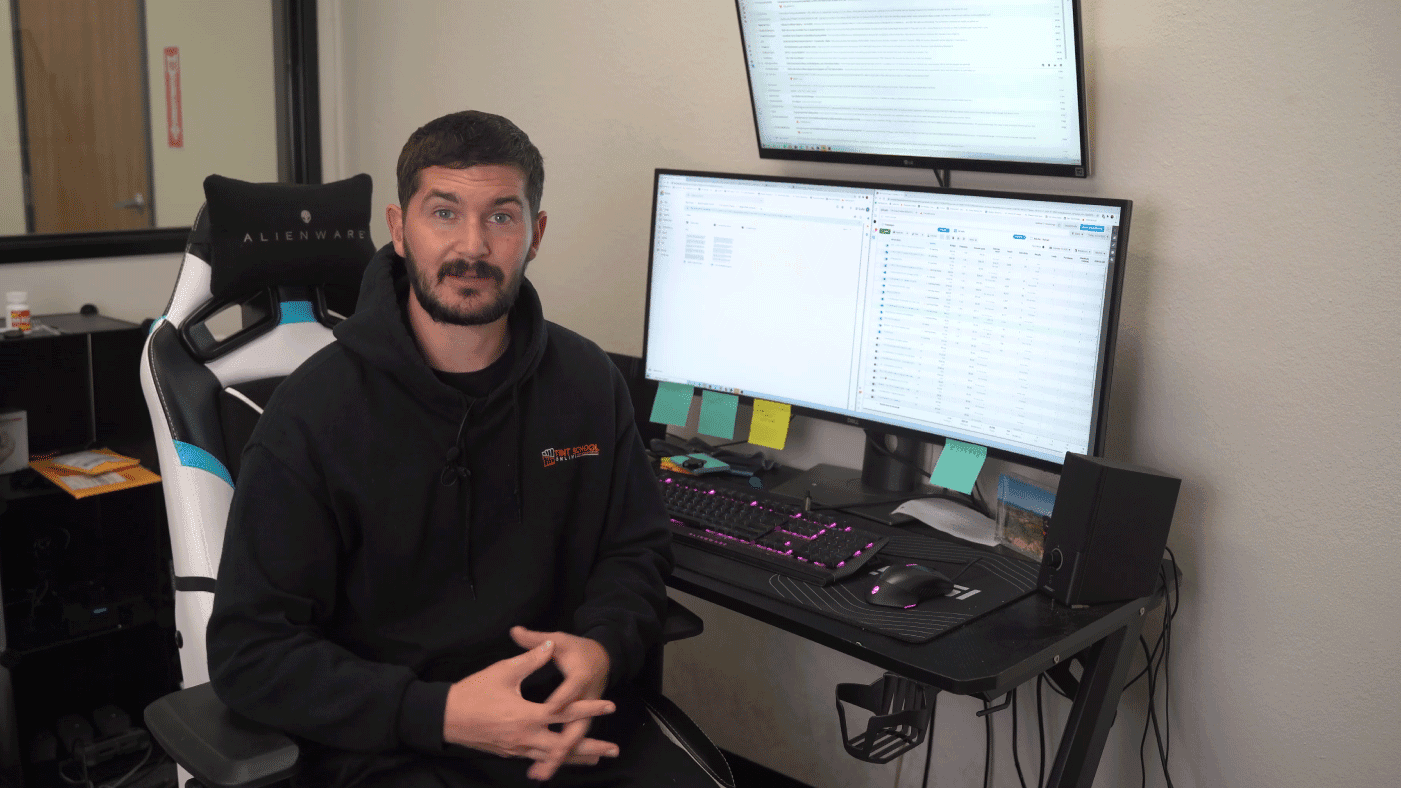 Elliot teaching business material at his desk with computer screens behind him
