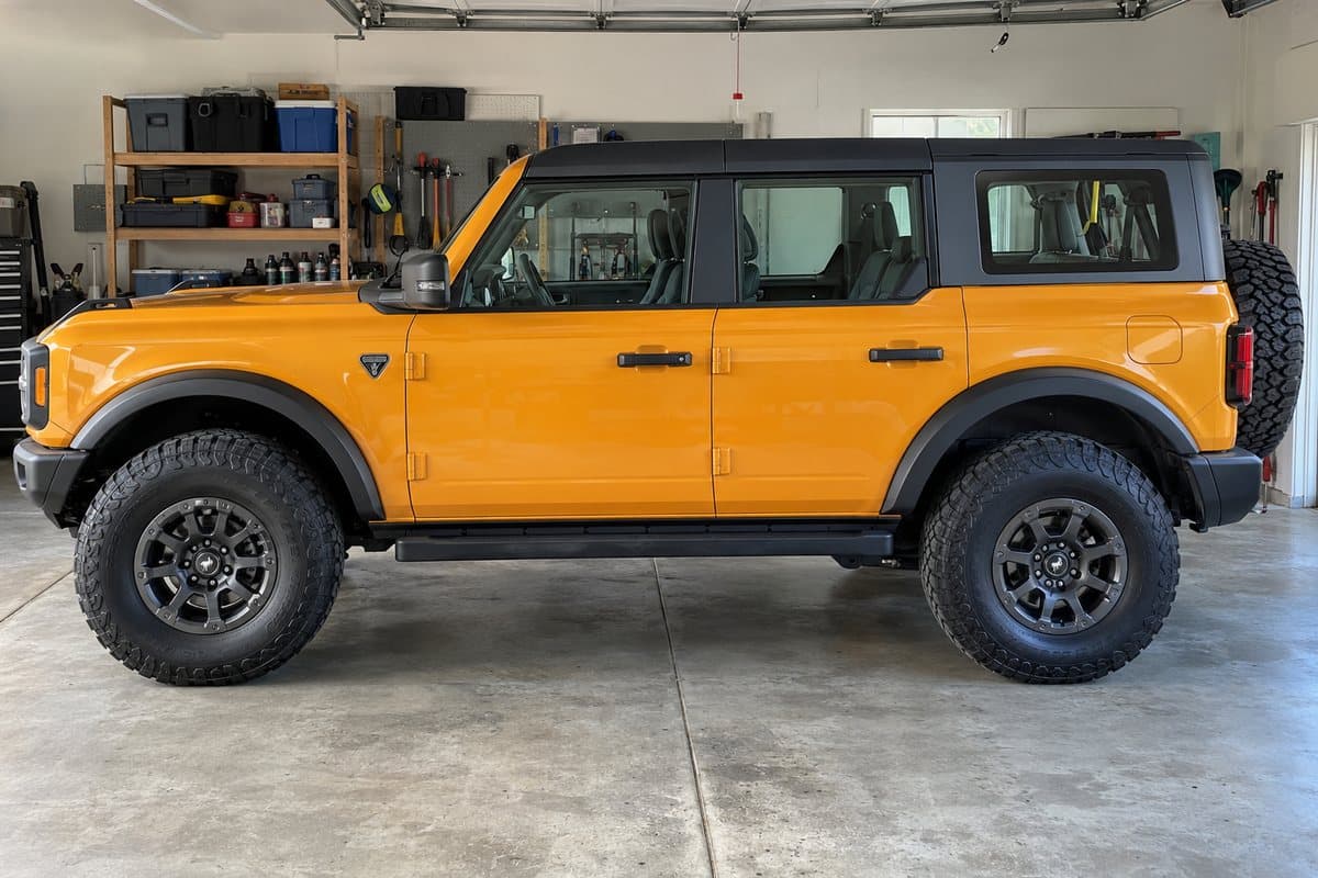 A bright orange Ford Bronco in a home garage, its windows half clear and half tinted