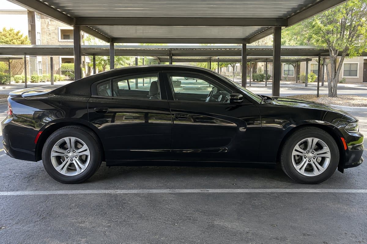 A black Dodge Charger under a covered carport, its windows half clear and half tinted